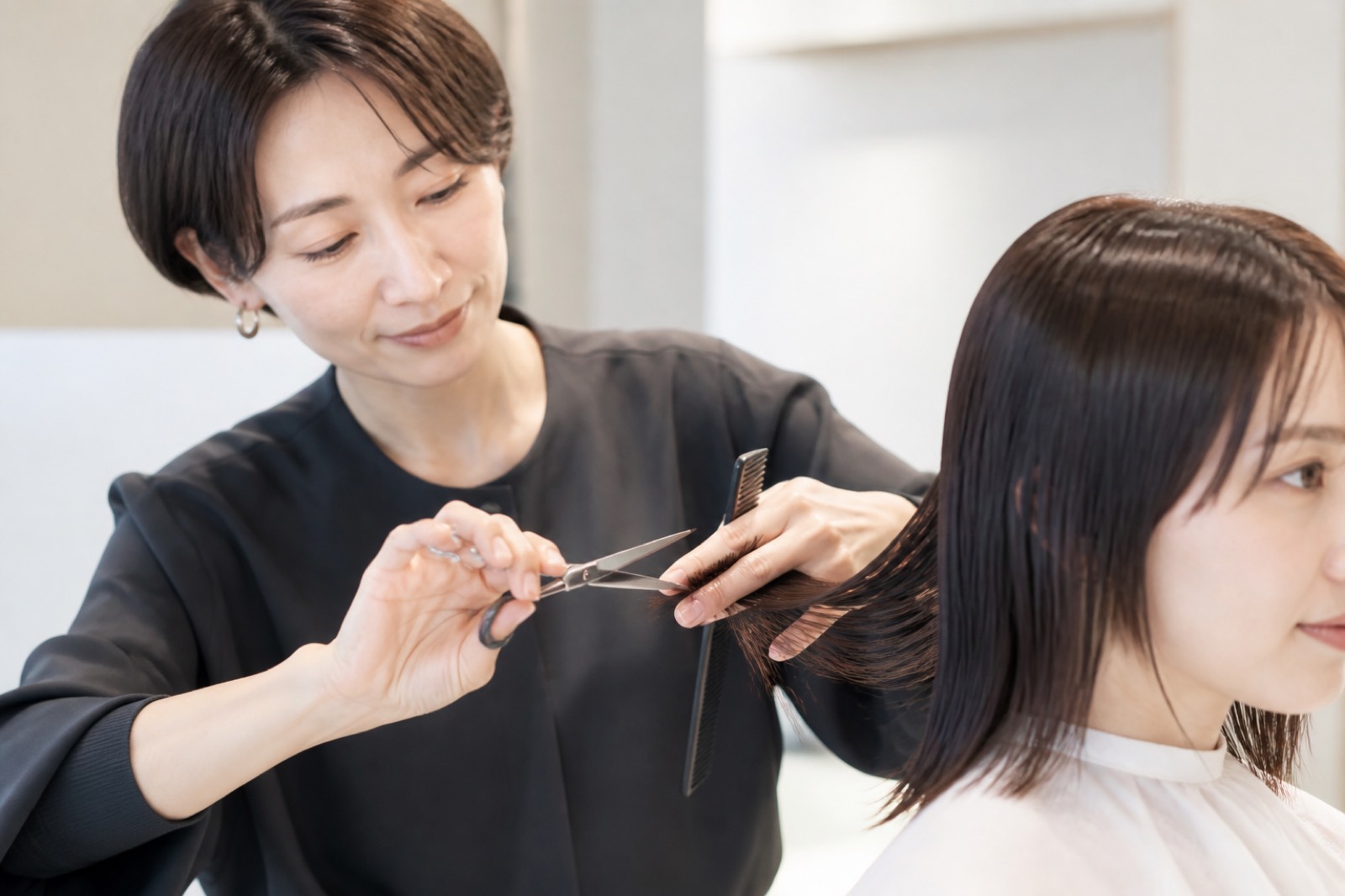 明るいサロンで女性客の髪を丁寧にカットする日本人スタイリスト