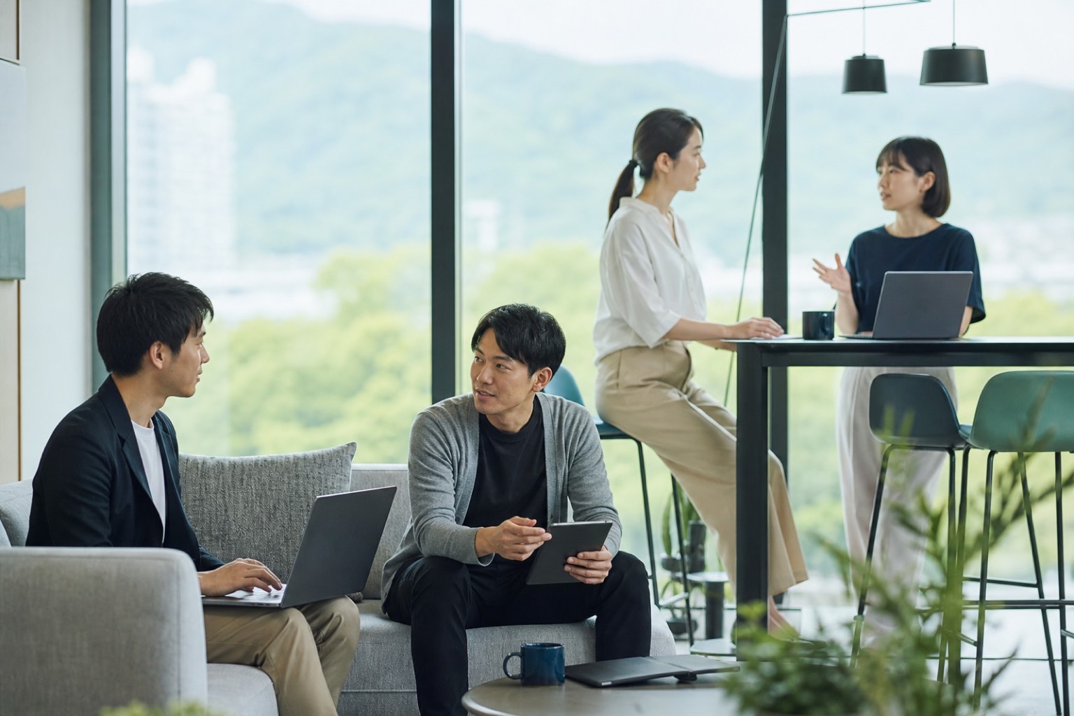 瀬戸内の景色が広がる明るいオフィスラウンジで会話する社員たち